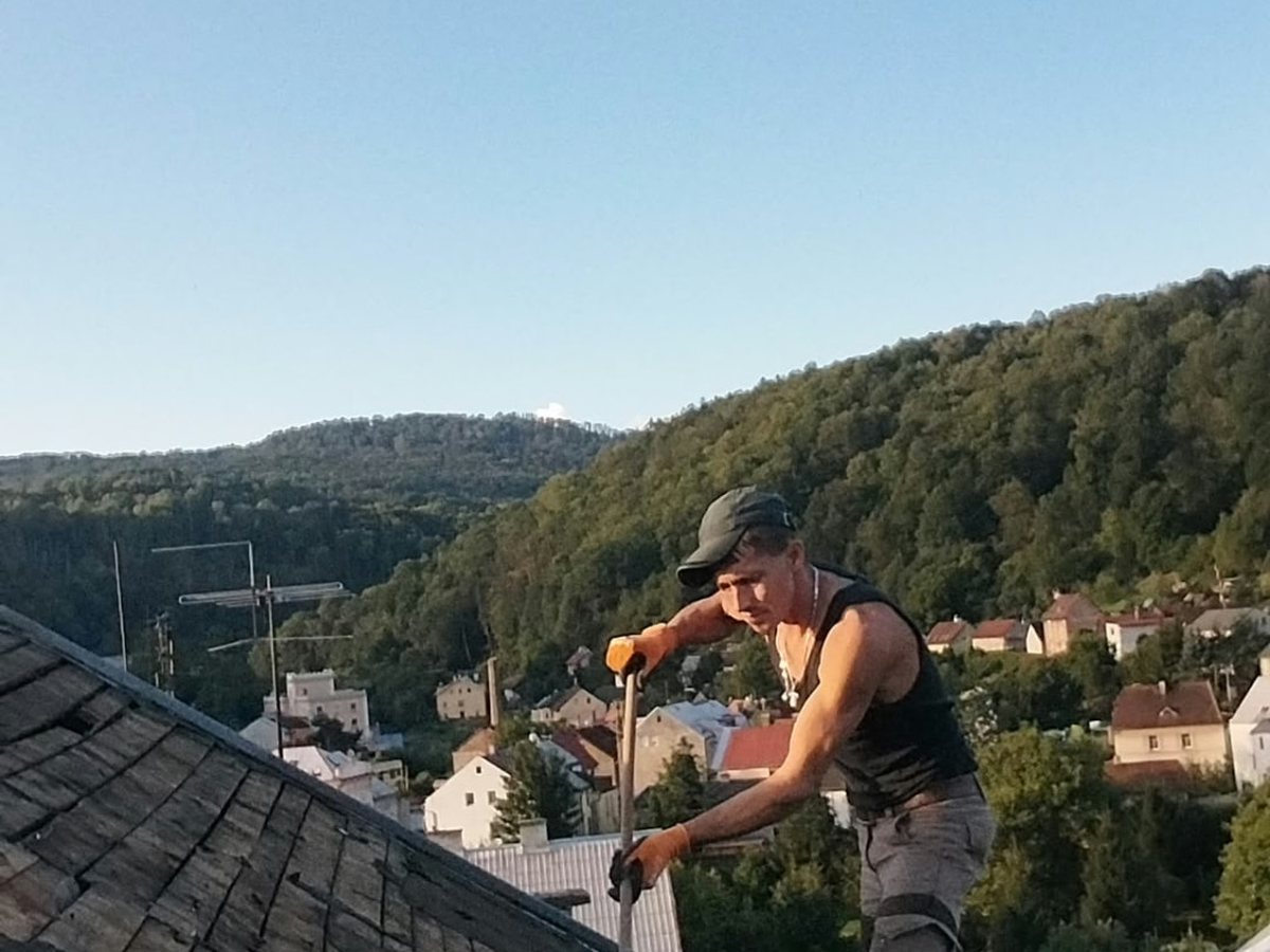 Výměna střešní krytiny — pracovník na hřebeni vysokého městského domu
